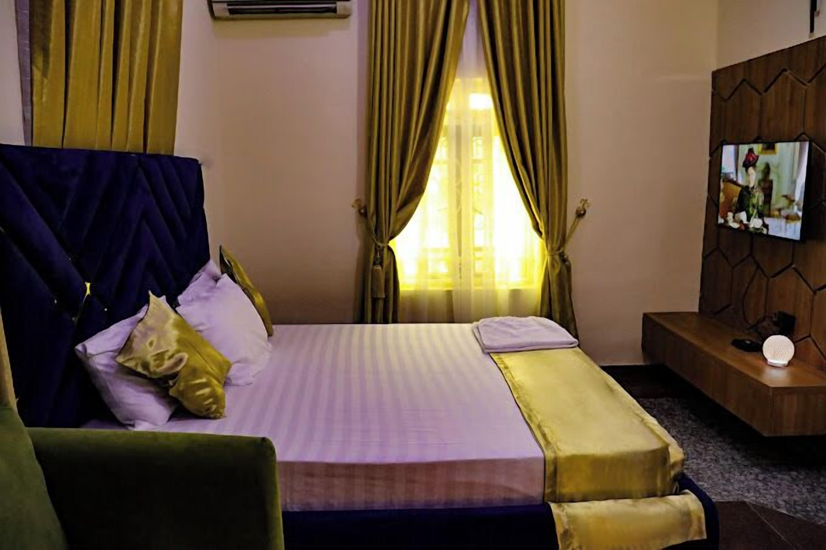 Une chambre d’hôtel avec un lit, un téléviseur fixé au mur en bois et une fenêtre avec des rideaux.