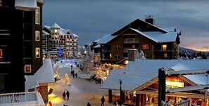A snow-covered town square with buildings, including a lodge with a thatched roof and a multi-story hotel with a ski lift visible in the background. - NEW! Seneca 113: Private Entrance, Hot Tub, Heated Garage, Sleeps 6! (Snowshoe)
