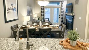 A modern kitchen with granite countertops, a dining area with a dark wood table and chairs, a built-in oven, and a fireplace. - NEW! Seneca 113: Private Entrance, Hot Tub, Heated Garage, Sleeps 6! (Snowshoe)