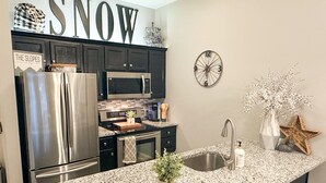 A modern kitchen with stainless steel appliances, a granite countertop, and a decorative wall sign that reads "SNOW". - NEW! Seneca 113: Private Entrance, Hot Tub, Heated Garage, Sleeps 6! (Snowshoe)