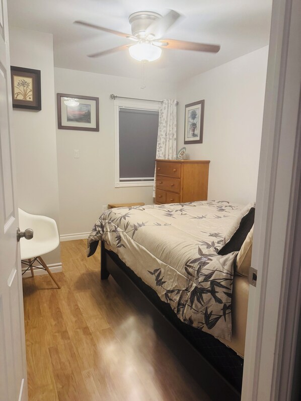 A bedroom with a bed, a ceiling fan, a window with curtains, a dresser, and a chair.