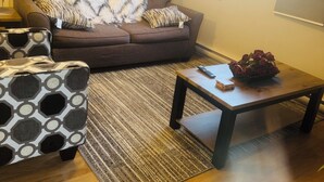 A living room with a brown sofa, patterned ottoman, and a coffee table with a vase of flowers.