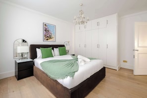 A bedroom with a bed, nightstand, dresser, wardrobe, chandelier, and a framed picture on the wall.
