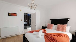 Une chambre à coucher avec un grand lit, un lustre, un radiateur et une porte donnant sur un balcon.