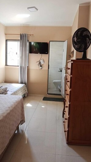 Quarto com cama, televisão, ventoinha e cómoda de madeira.