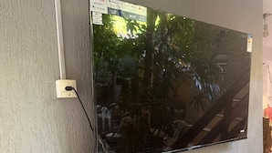 A flat-screen TV mounted on a textured wall, with a remote and a decorative item below it. - Pousada Plantar e Cuidar (Santa Cruz do Escalvado)