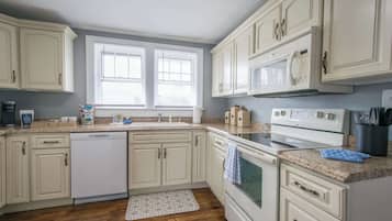 Une cuisine avec des meubles blancs, un lave-vaisselle, une cuisinière et un four à micro-ondes.