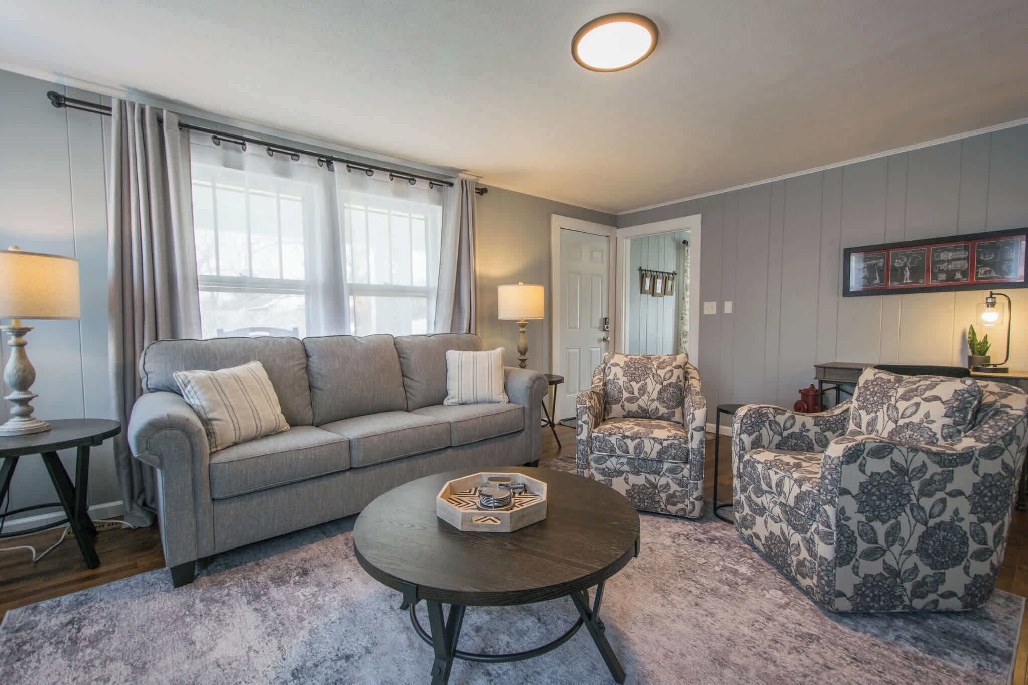 Ein Wohnzimmer mit grauem Sofa, einem gemusterten Sessel und einem Couchtisch.