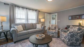 Ein Wohnzimmer mit grauem Sofa, einem gemusterten Sessel und einem Couchtisch.