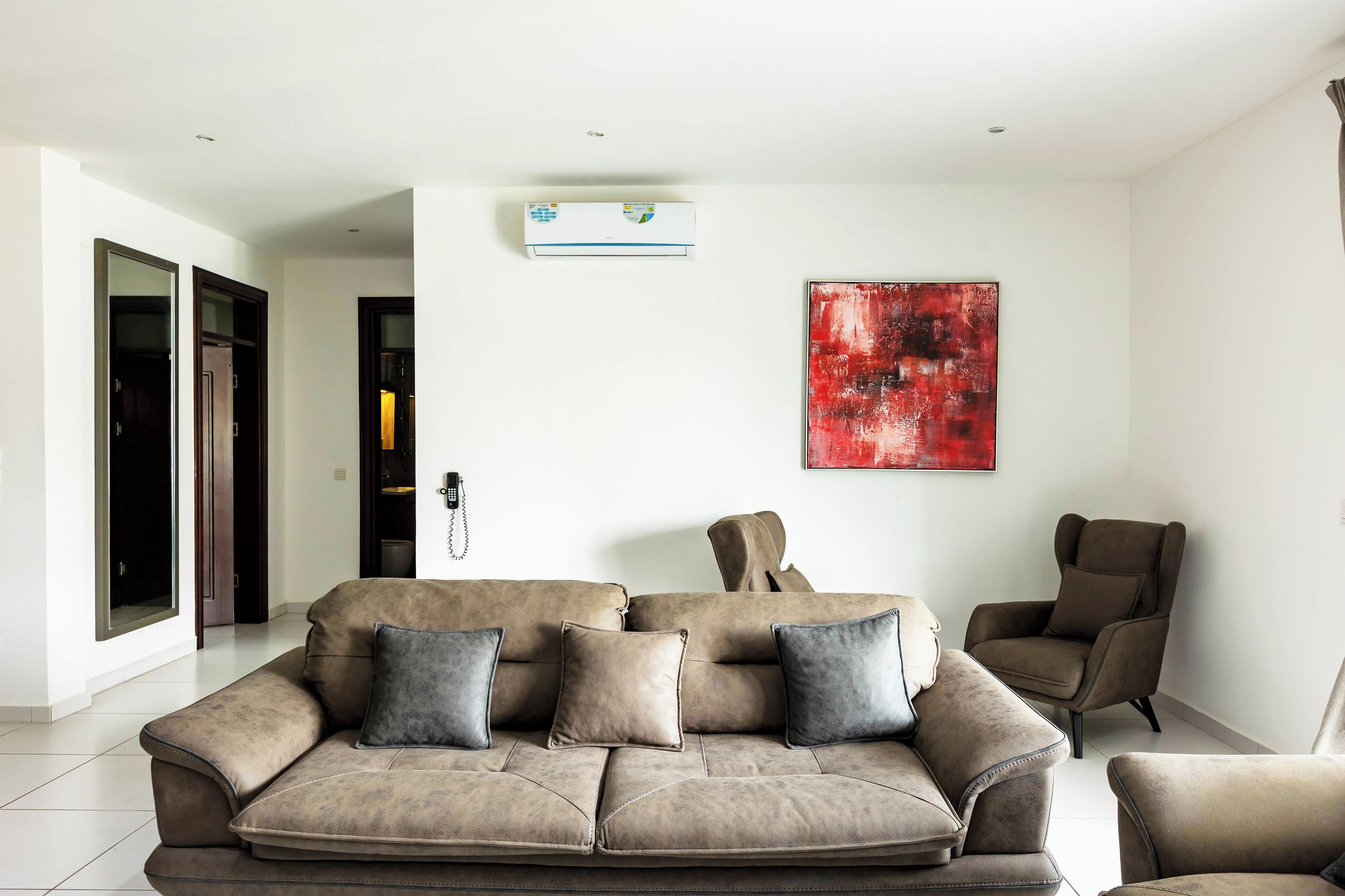 A modern living room with a beige sectional sofa, a brown armchair, and a red abstract painting on the wall.