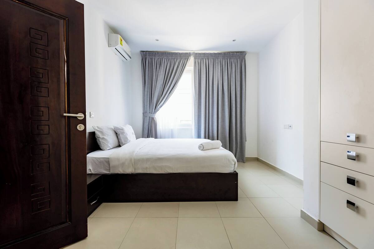 Une chambre à coucher avec un lit, une armoire, une porte et une fenêtre avec des rideaux.
