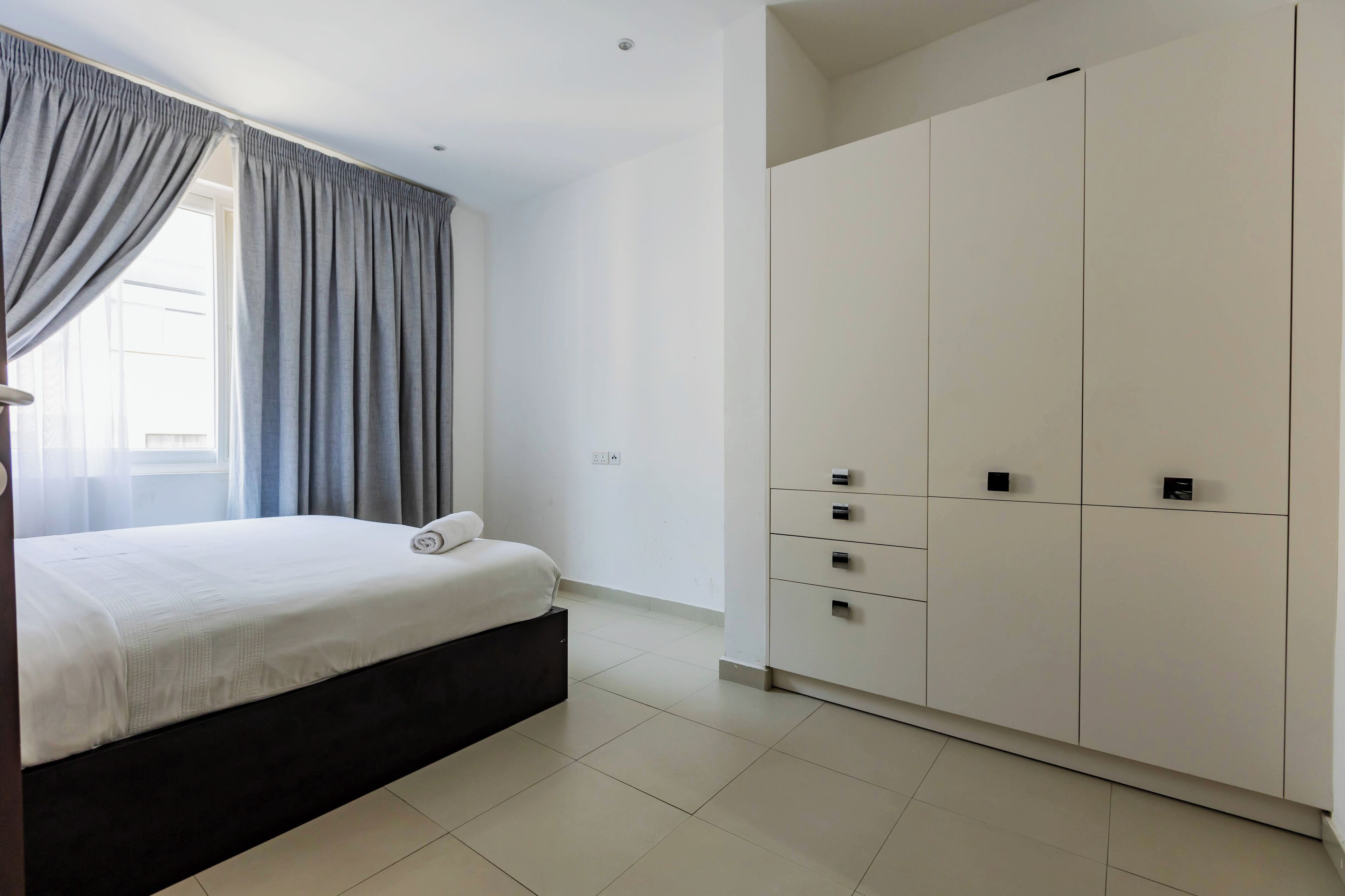 A bedroom with a bed, a wardrobe, and a window with curtains.