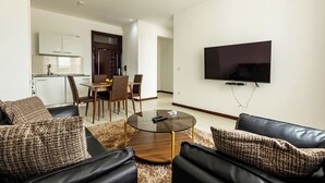 A modern living room with a glass coffee table, leather sofas, and a flat-screen TV mounted on the wall.