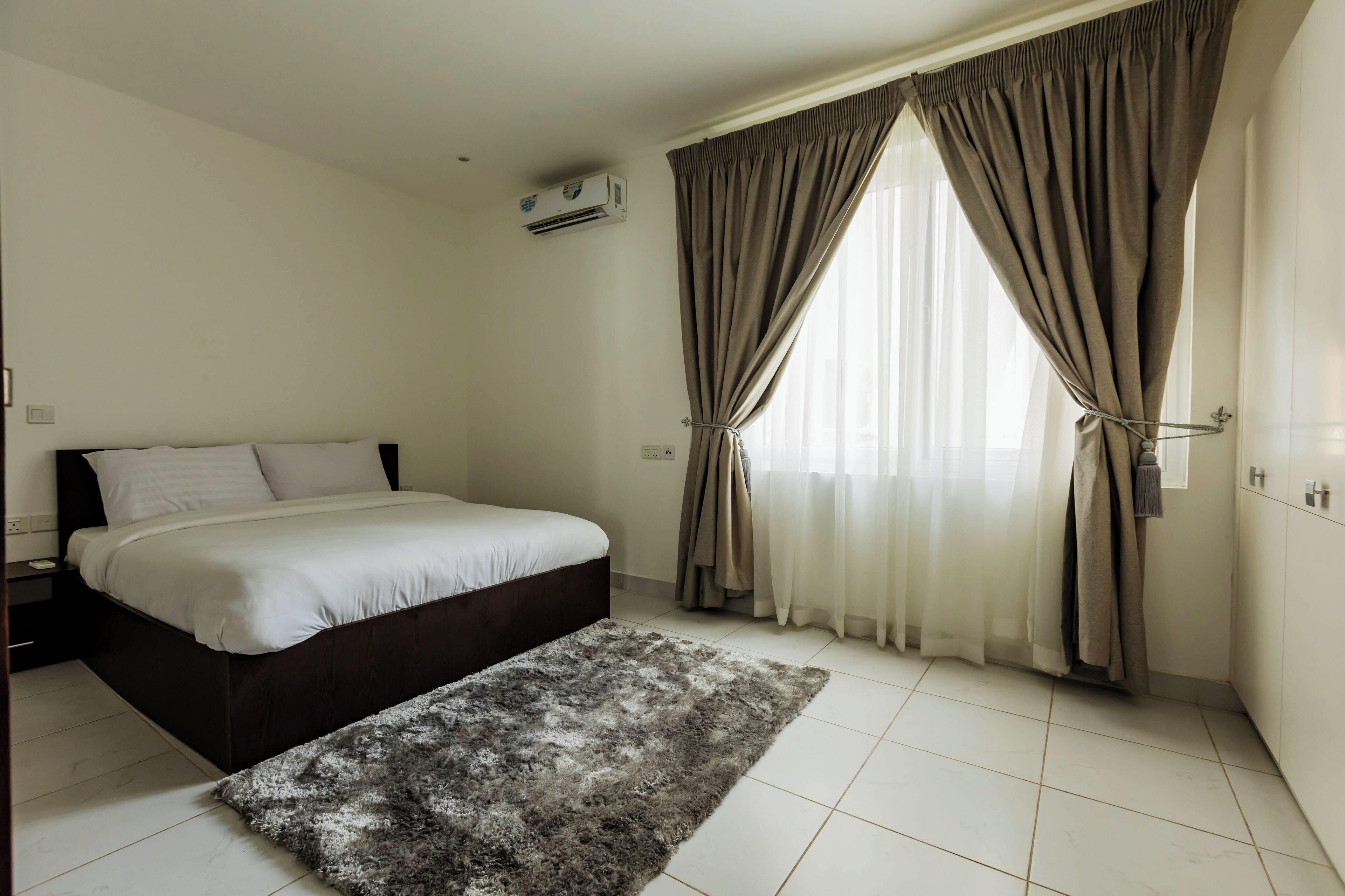 Quarto com cama, cortinas, ar condicionado e tapete.