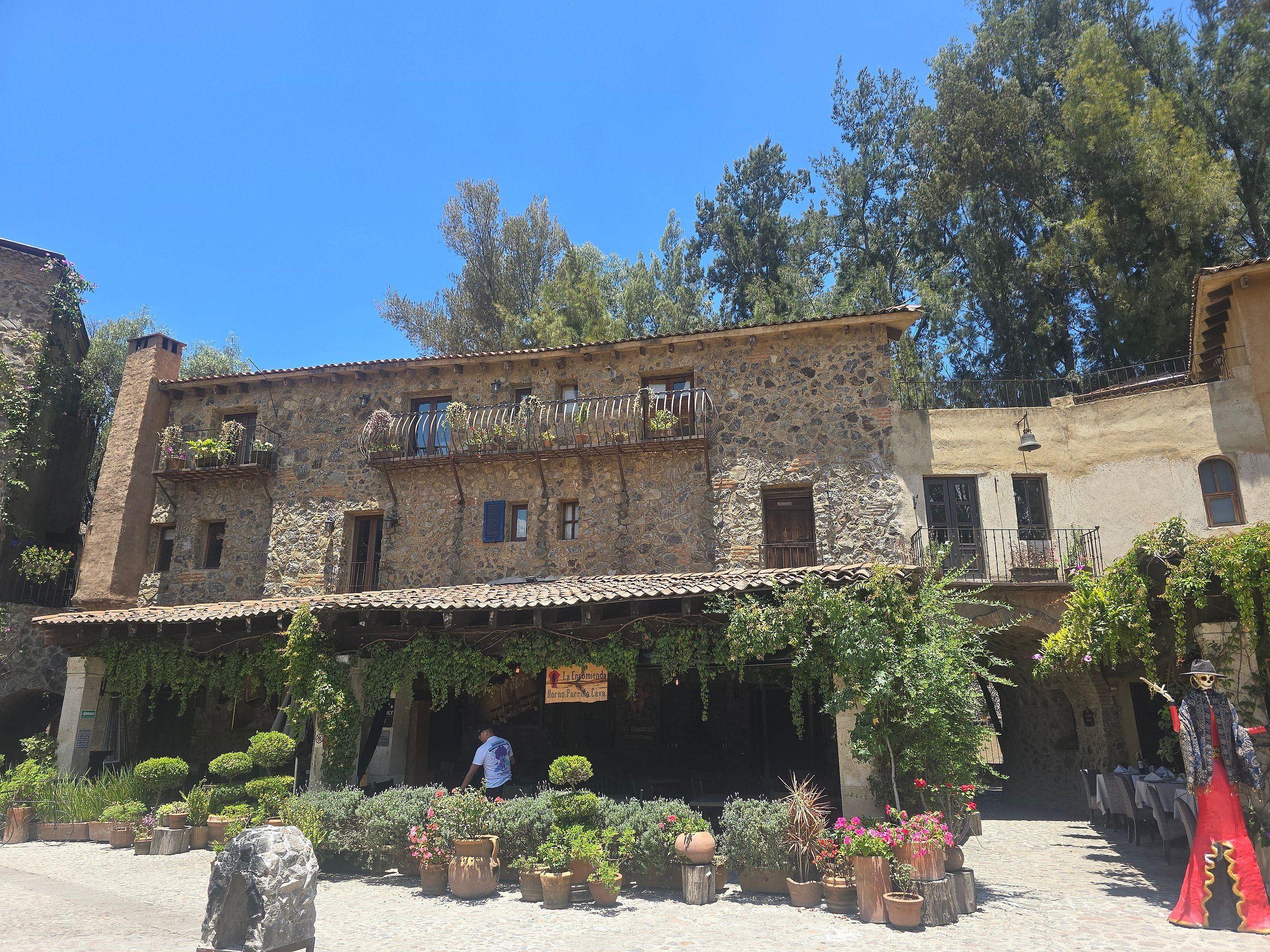 A stone building with a balcony, surrounded by potted plants and a cobblestone courtyard.