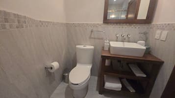 A bathroom with a toilet, sink, mirror, and tiled walls.
