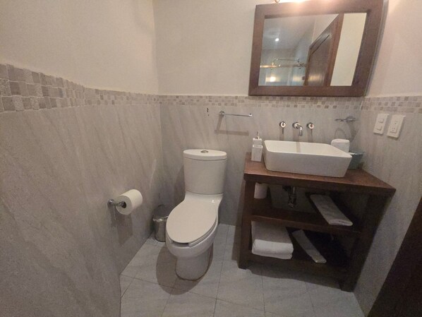 A bathroom with a toilet, sink, mirror, and tiled walls.