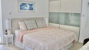Een slaapkamer met een bed, een nachtkastje met een lamp, een ingelijst schilderij aan de muur en een schuifdeur voor een kast.