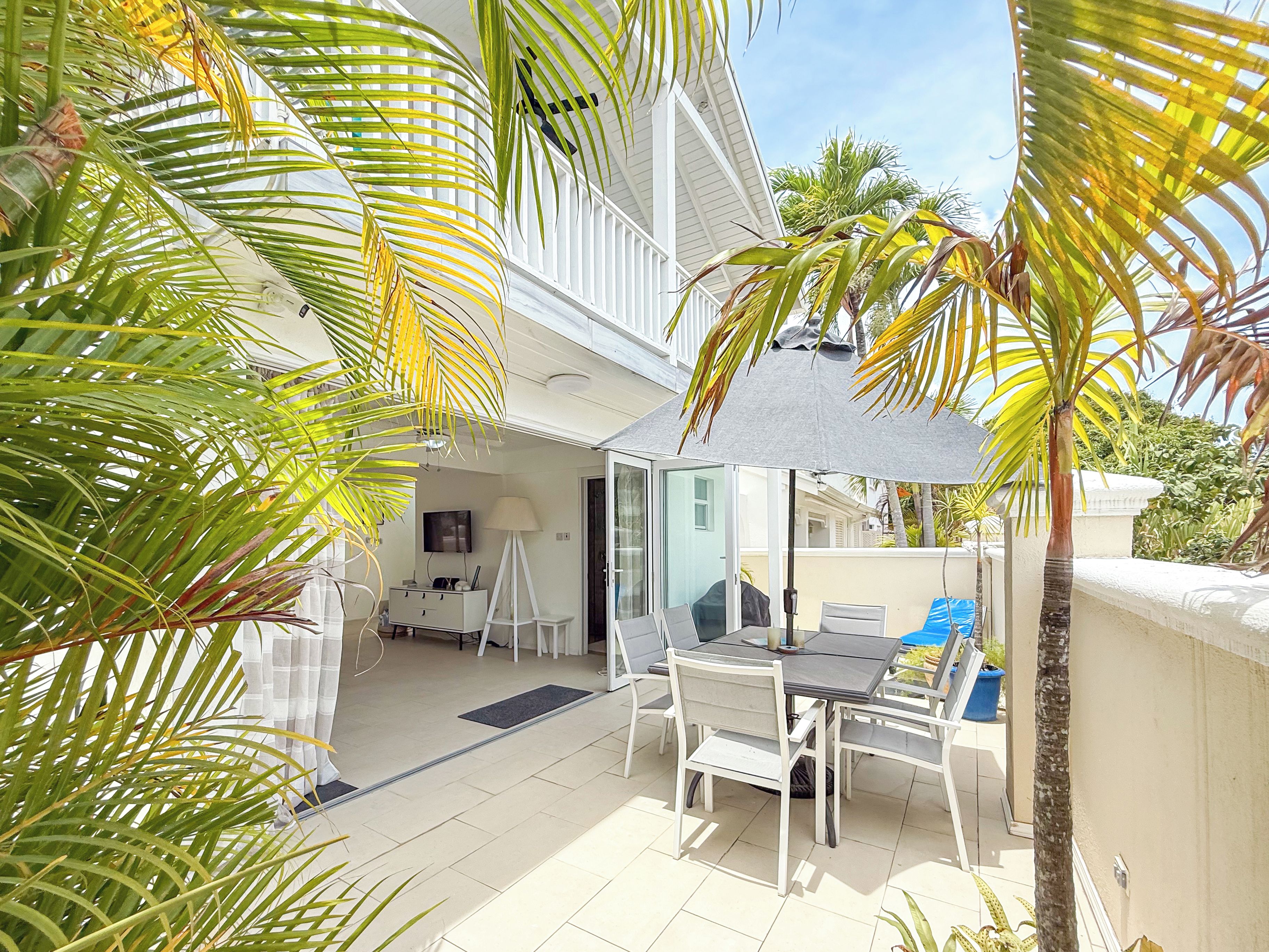 A patio with a table and chairs, surrounded by palm trees and a white railing.