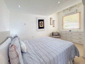 Ein Schlafzimmer mit einem Bett, einem Sessel, einem Schminktisch und einem Fenster mit Jalousien.