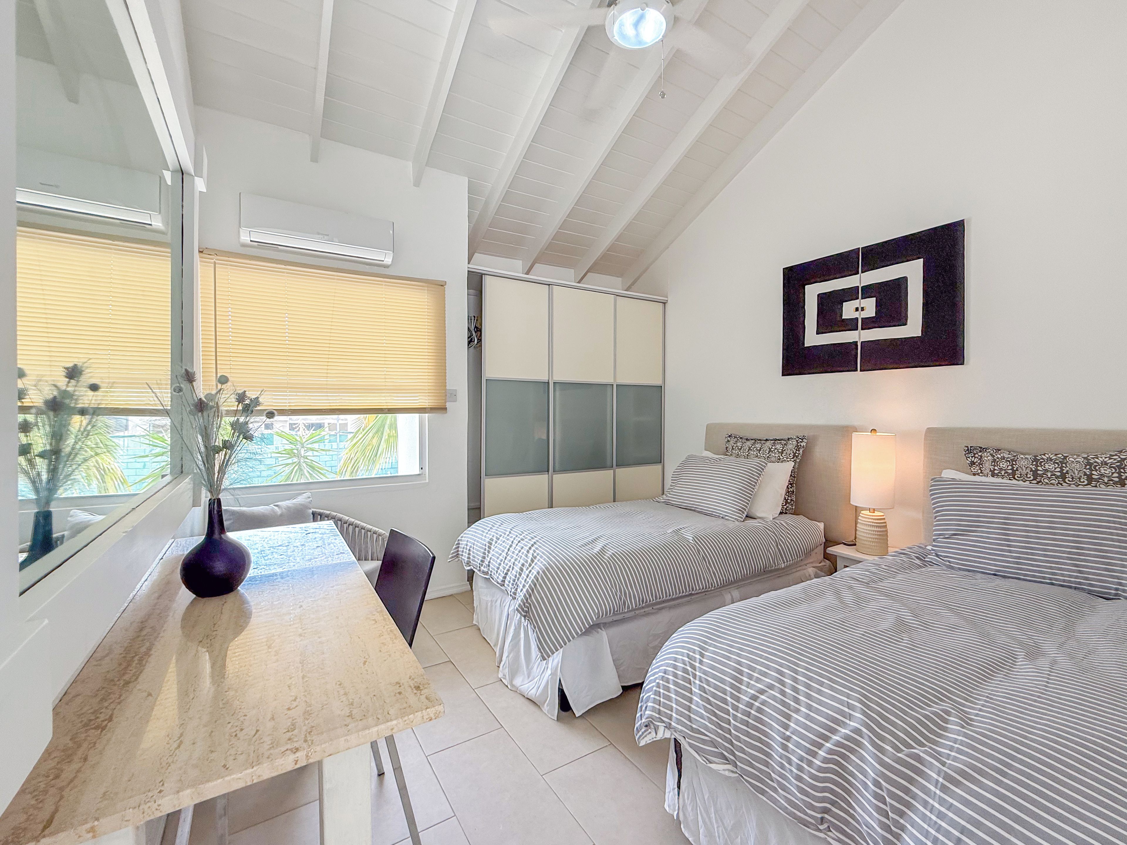 A bedroom with two beds, a desk, and a window with blinds.