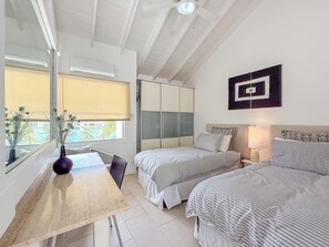 A bedroom with two beds, a desk, and a window with blinds.