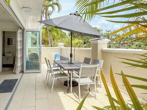 Eine Außenpatio mit Tisch und Stühlen, einem schwarzen Sonnenschirm und Blick auf einen Garten mit Palmen.