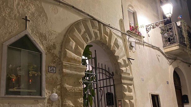 A historic building with a large arched entrance, a small window with a cross, and a balcony with plants. - A CASA DI BARBARA A love nest in the heart of Galatina (Galatina)