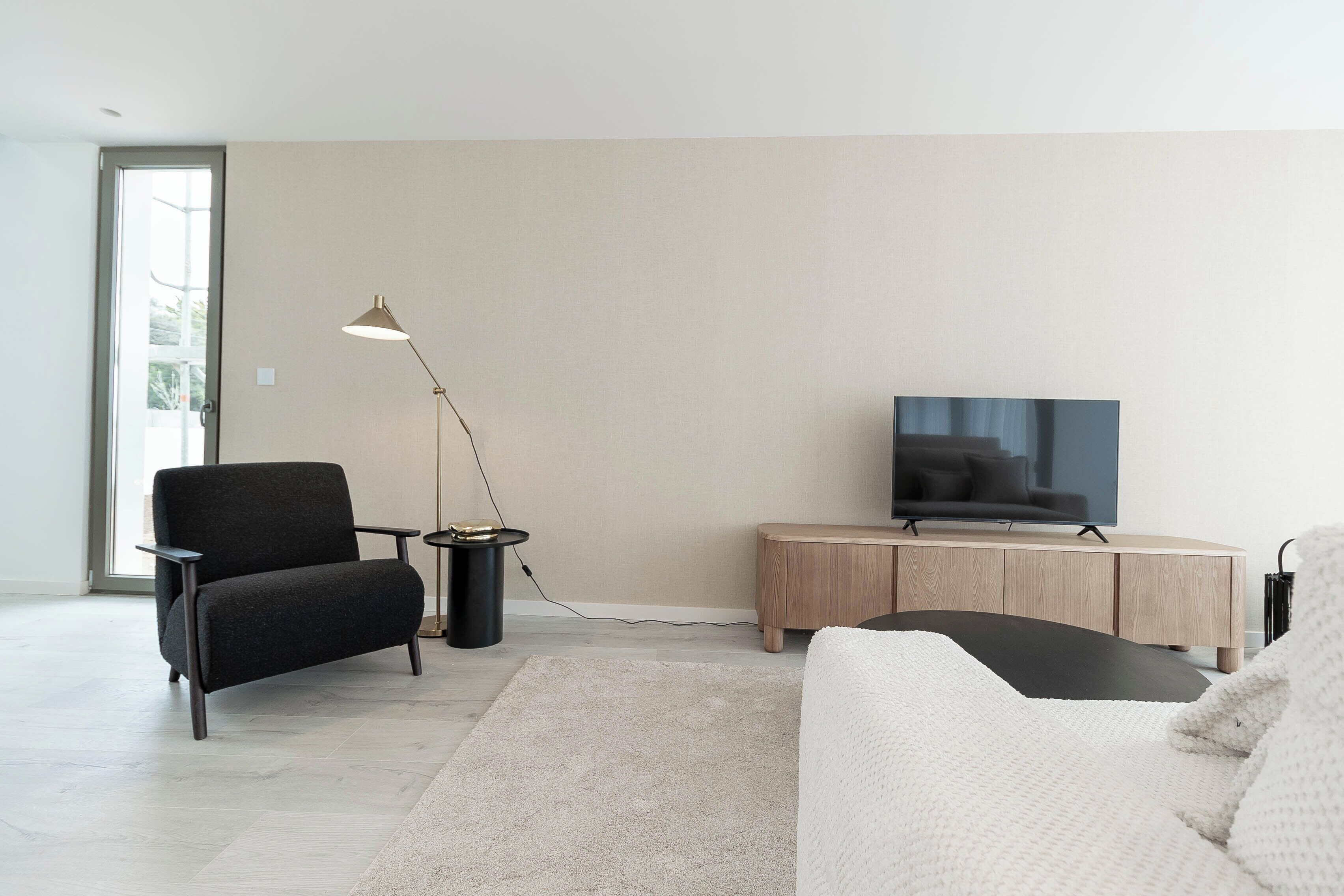 A modern living room with a sofa, a TV, a lamp, and a small side table.