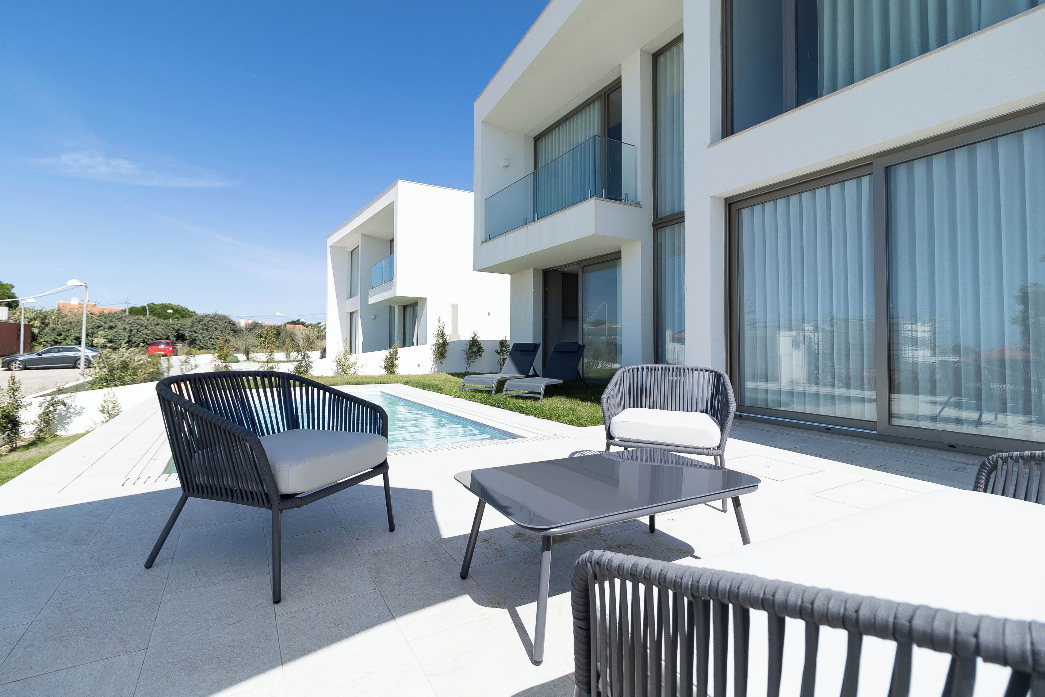 A modern outdoor patio with a pool, lounge chairs, and a glass table.