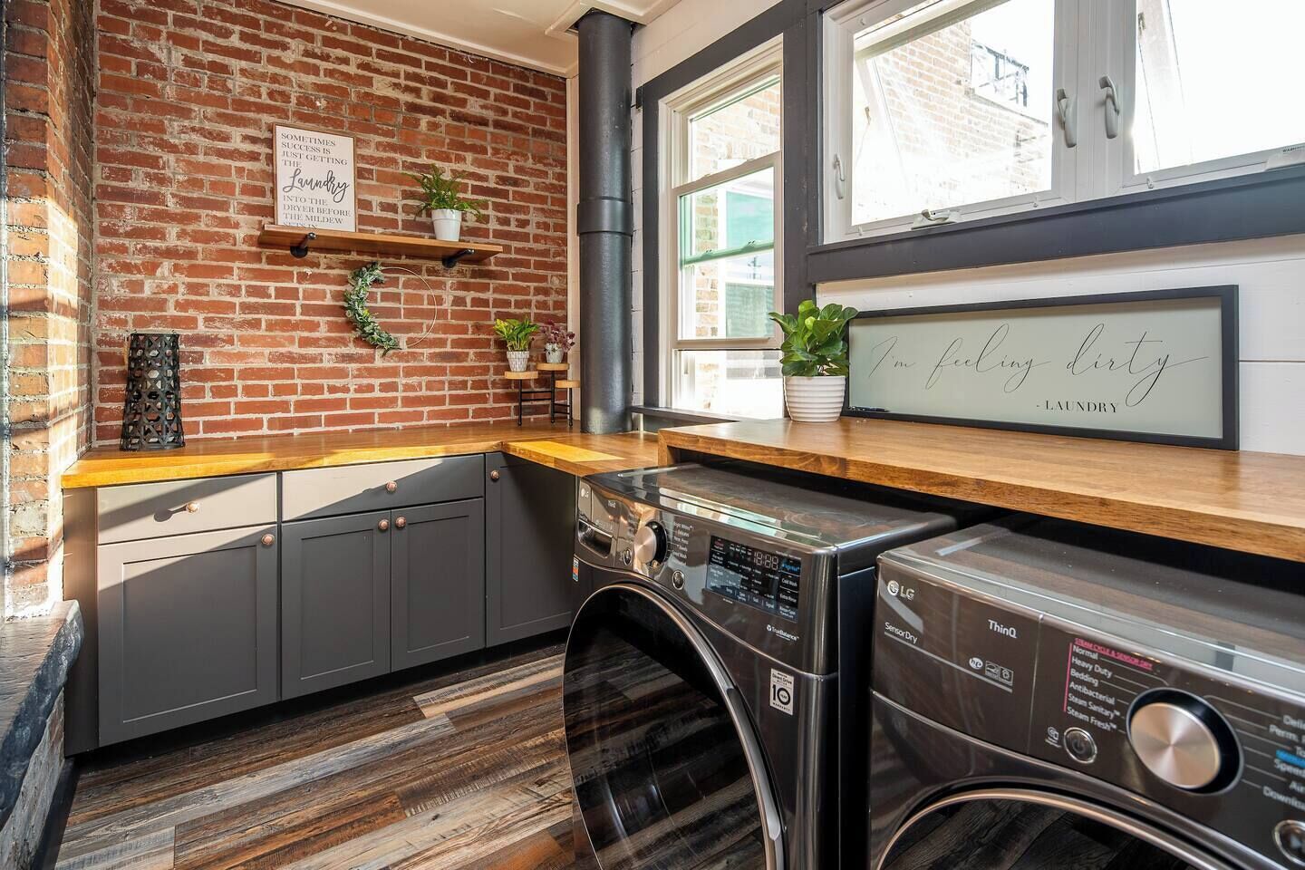 A laundry area with a brick wall, wooden shelves, and a large window.