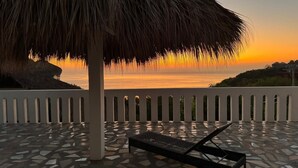 Eine Terrasse mit einem Reetdach, einem gemusterten Boden und Blick auf den Sonnenuntergang über dem Meer.