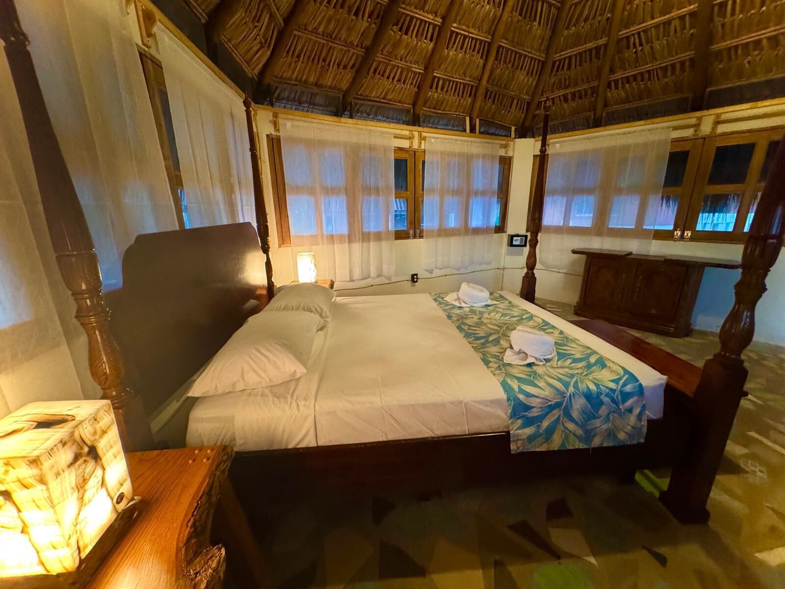 Une chambre avec un lit, une table de chevet, une tête de lit en bois et un toit de chaume.