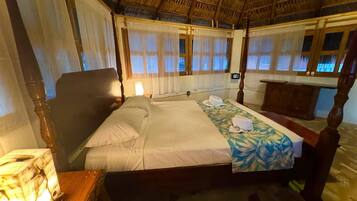Une chambre avec un lit, une table de chevet, une tête de lit en bois et un toit de chaume.