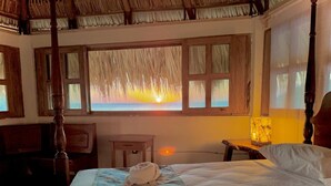 Ein Schlafzimmer mit Bett, Nachttisch, Lampe und Fenster mit Sonnenuntergangsblick.
