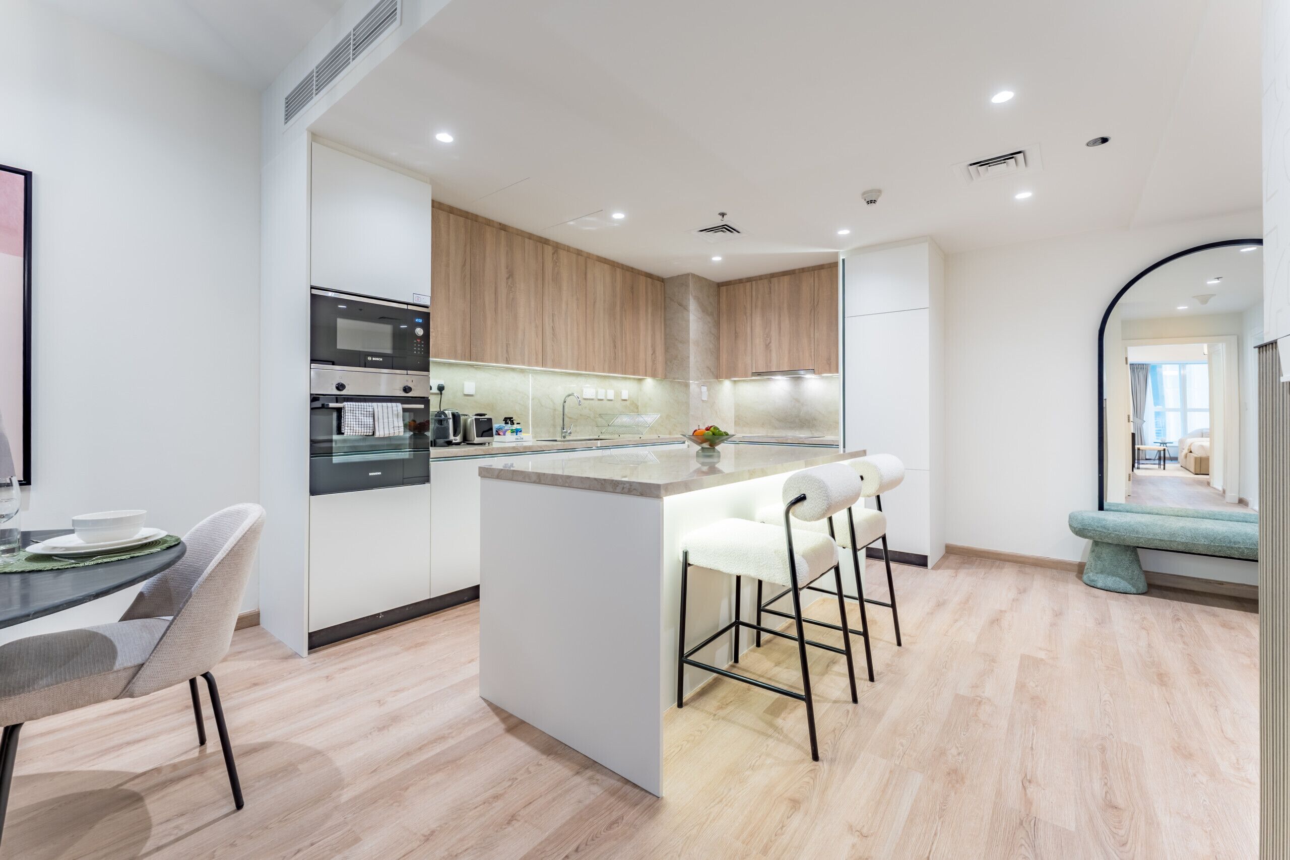A modern kitchen with a central island, bar stools, and a dining area with a table and chairs.