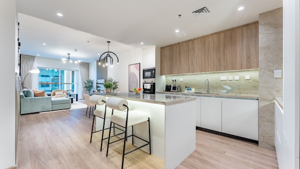 A modern kitchen with a central island, bar stools, and a dining area with a sofa and coffee table.