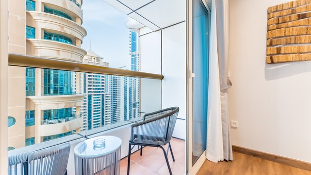 A balcony with a view of high-rise buildings, a small table, and two chairs. - Upgraded 2BR with Partial Sea and City Views Near the Beach, Elite Residence (Dubai)