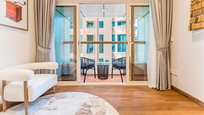 A modern living room with a sofa, a round rug, and a view of an outdoor balcony with a table and chairs. - Upgraded 2BR with Partial Sea and City Views Near the Beach, Elite Residence (Dubai)