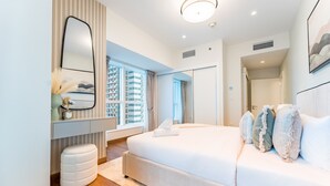 A modern bedroom with a large bed, a bedside table, a mirror, and a window with a city view. - Upgraded 2BR with Partial Sea and City Views Near the Beach, Elite Residence (Dubai)