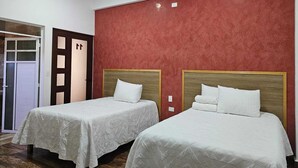Ein Hotelzimmer mit zwei Betten, einer roten Wand mit Struktur und einer Holztür mit Fensterteil.
