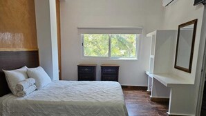 Ein Hotelzimmer mit zwei Betten, einem Fenster mit Blick auf Grünflächen, einem weißen Schminktisch mit Spiegel und einem Holzkopfteil.