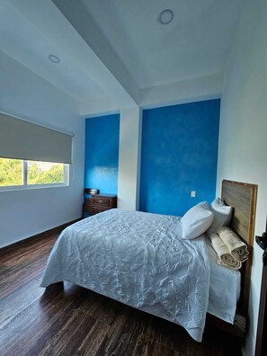 A bedroom with a large bed, a wooden headboard, and a window with a view of greenery. - Hotel Familiar Abejac (Puerto Escondido)