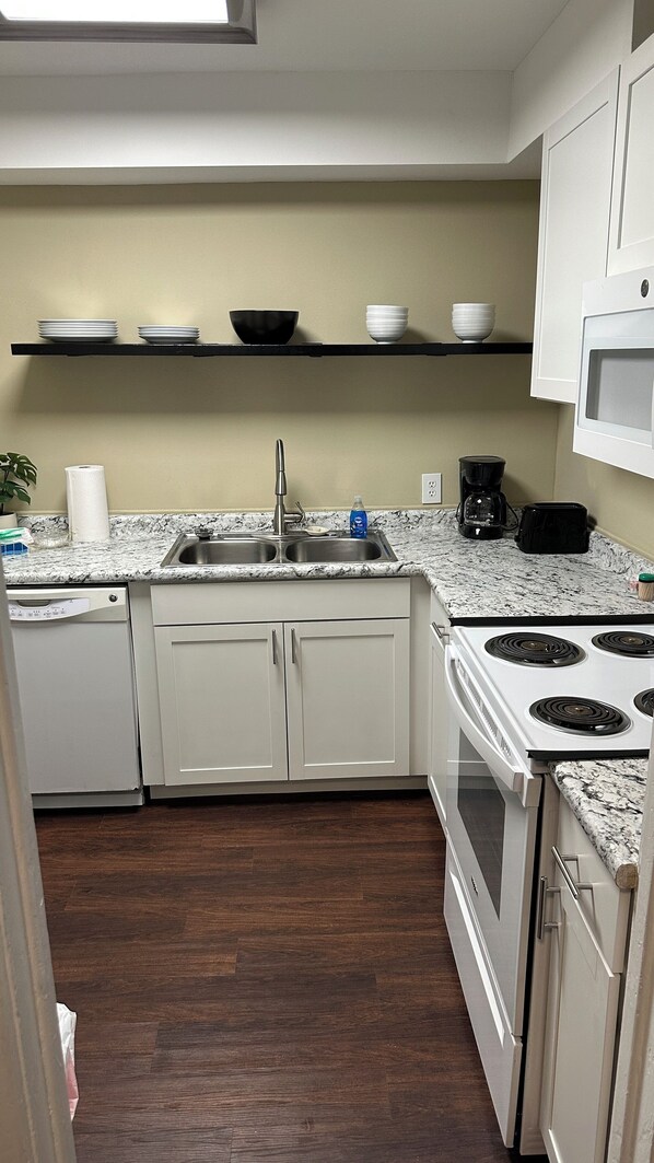 A modern kitchen with white cabinetry, a granite countertop, a stainless steel sink, a microwave, and a stove.