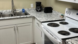 A kitchen with white cabinets, a white stove, a microwave, and a granite countertop. - The Greenfield: 2-bedroom townhome close to LSU (Baton Rouge)