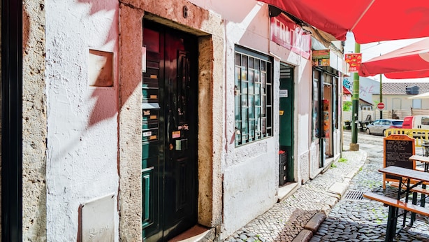 A narrow street with cobblestone pavement, a row of shops with red awnings, and a signboard with text. - Alfama Vibes Apartments (Lisbon)