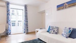 A room with a white sofa, patterned pillows, a dark rug, and a painting of a historical building on the wall. - Alfama Vibes Apartments (Lisbon)