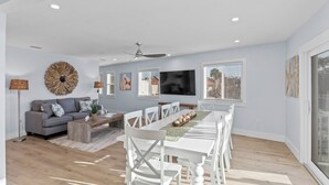A modern living room with a grey sofa, white chairs, a dining table, and a TV.