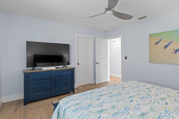 A bedroom with a bed, a dresser, a television, and a ceiling fan.