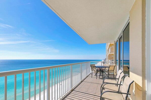 A balcony with a view of the ocean, a table with chairs, and a building with balconies.